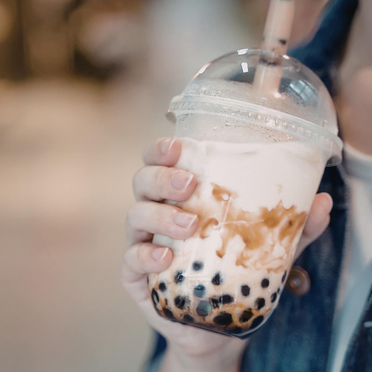 Takeaway brown sugar milk tea in plastic cup with creamy foam and tapioca pearls, popular café style bubble tea drink