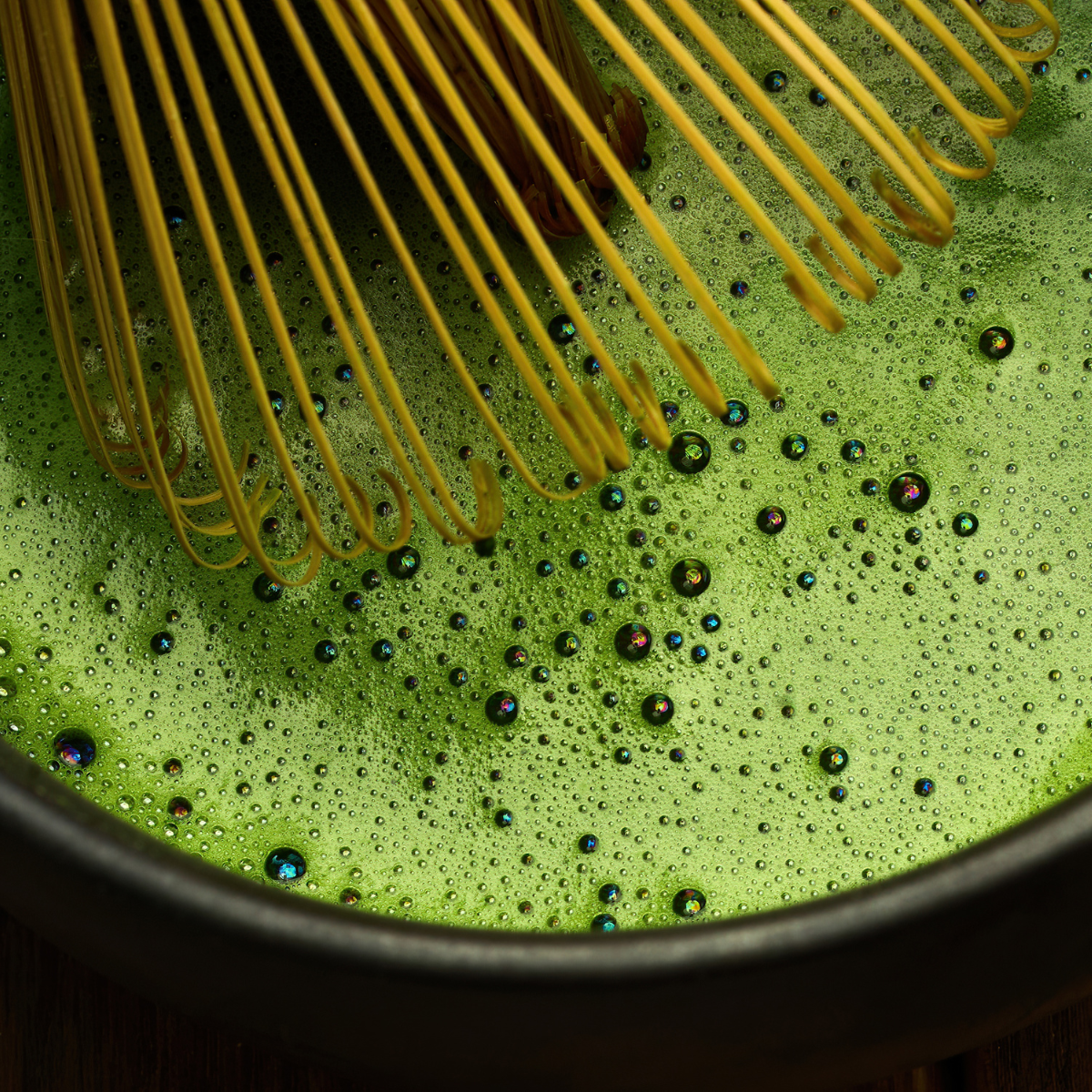 matcha powder being whisked into green tea mixture with foam for latte and beverage preparation