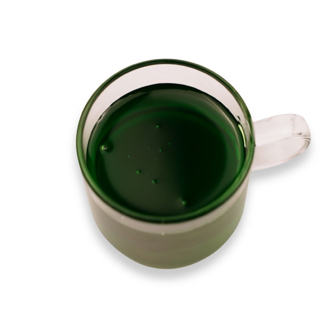 Dark green apple flavored syrup in a glass cup on a white background