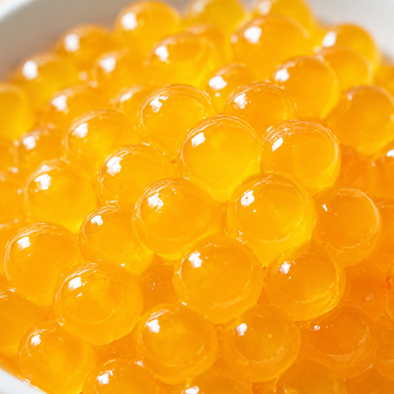 Close-up of Frubo Mango Popping Boba bursting juice pearls with vibrant golden color and tropical mango flavor